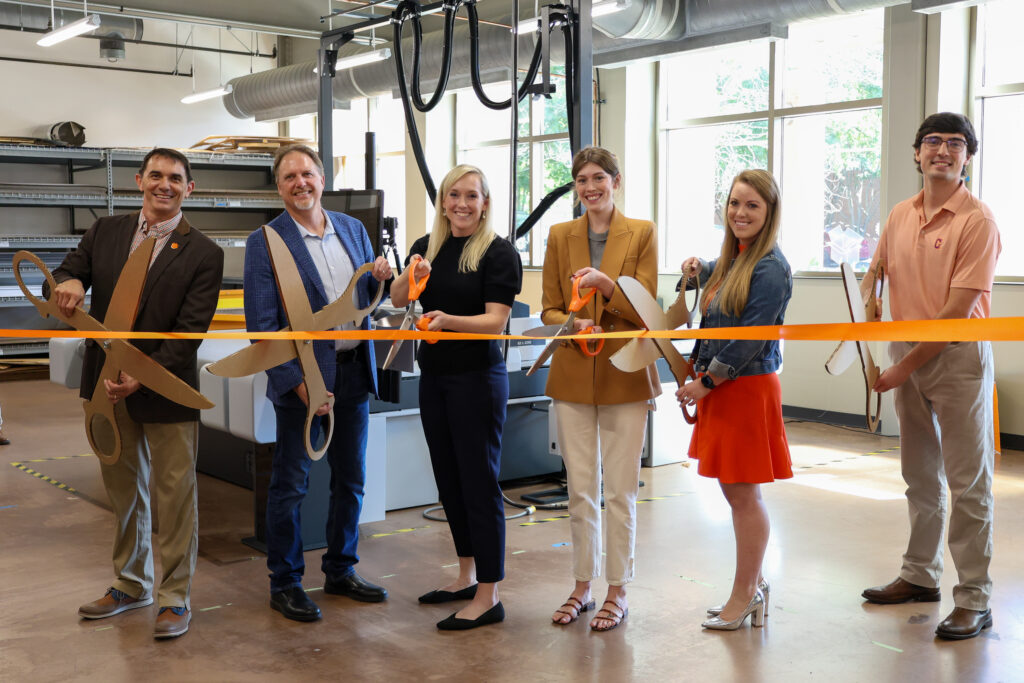 Employees, professors and student stand in front of brand new machinery during ribbon cutting ceremony.